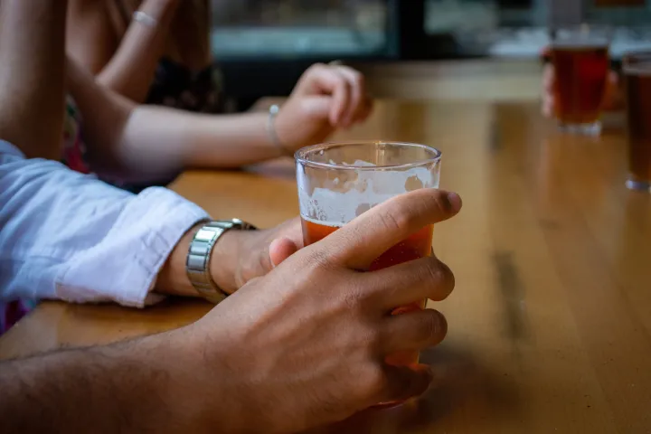 a hand holding a glass of beer on a table